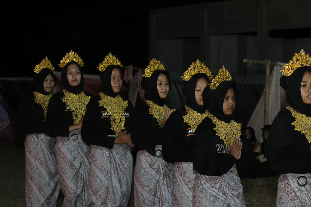 Peserta dengan busana dan hiasan kepala bernuansa emas dalam suasana penampilan malam