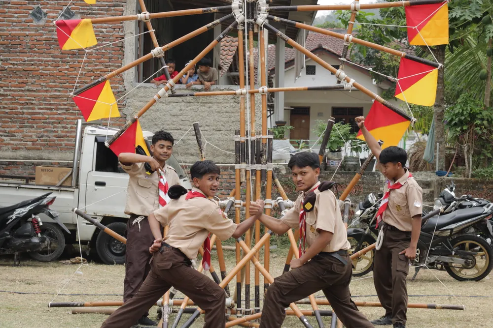 Peserta putra berpose di depan konstruksi tongkat dan tali yang dihiasi bendera kecil